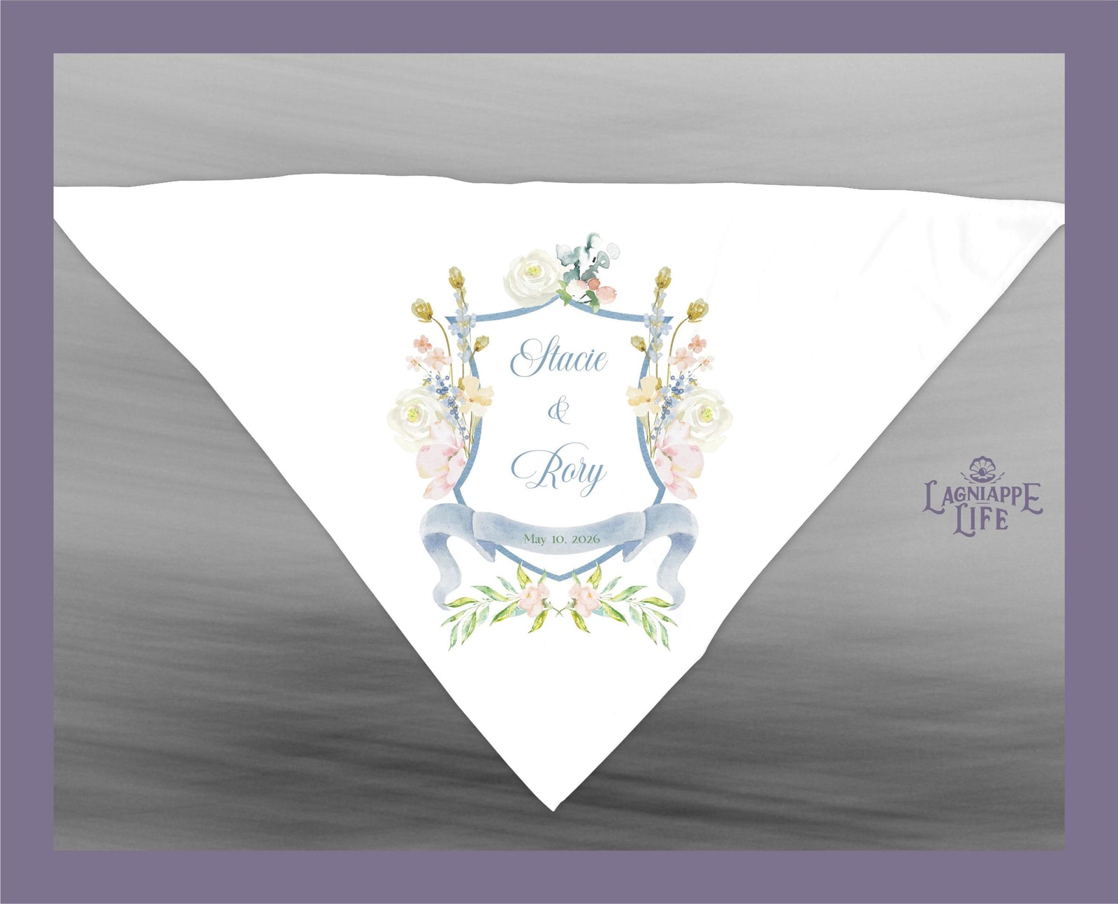 May include: A white wedding handkerchief with a blue and white floral design. The handkerchief has a blue shield with the text 'Stacie & Rory' and 'May 10, 2020' in the center. The shield is surrounded by a floral wreath. The text 'LAGNIAPPE LIFE' is in the lower right corner of the handkerchief.
