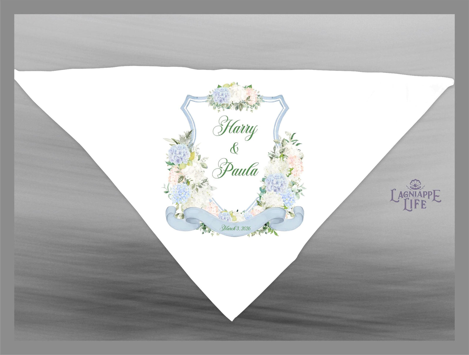 May include: A white wedding favor with a blue and white floral design. The favor features a crest with the words 'Harry & Paula' and the date 'June 01, 2018'. The favor is decorated with a blue ribbon and a green floral wreath. The bottom right corner of the favor has the words 'Lagniappe Life'.