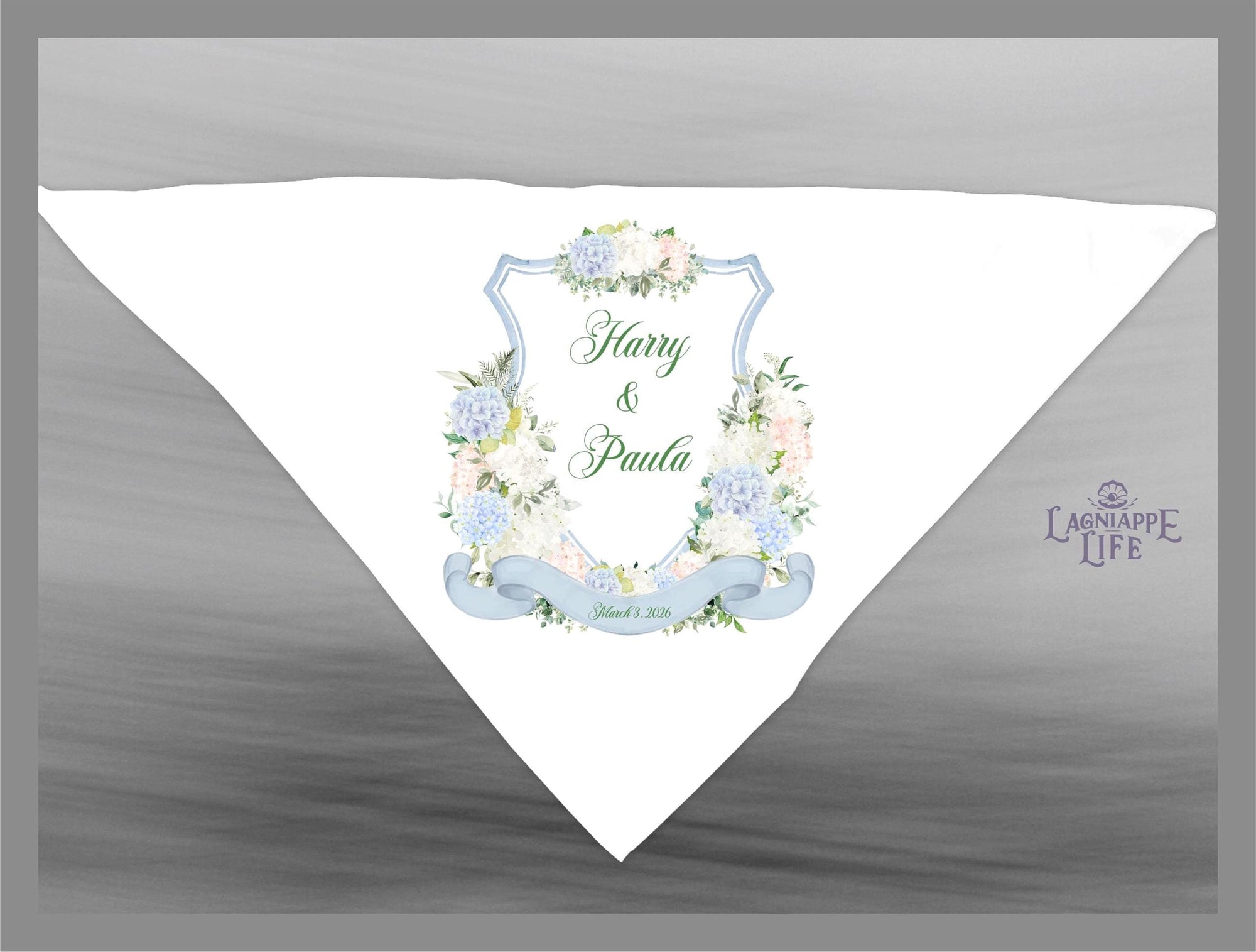 May include: A white wedding favor with a blue and white floral design. The favor features a crest with the words &#39;Harry & Paula&#39; and the date &#39;June 01, 2018&#39;. The favor is decorated with a blue ribbon and a green floral wreath. The bottom right corner of the favor has the words &#39;Lagniappe Life&#39;.
