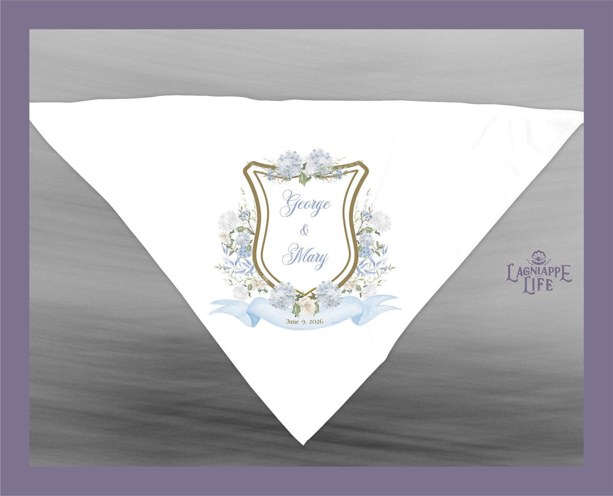 May include: A white wedding favor with a blue and gold crest. The crest has a floral design and the text 'George & Mary' and 'June 18, 2023'. The favor has the text 'Lagniappe Life' in the bottom right corner.