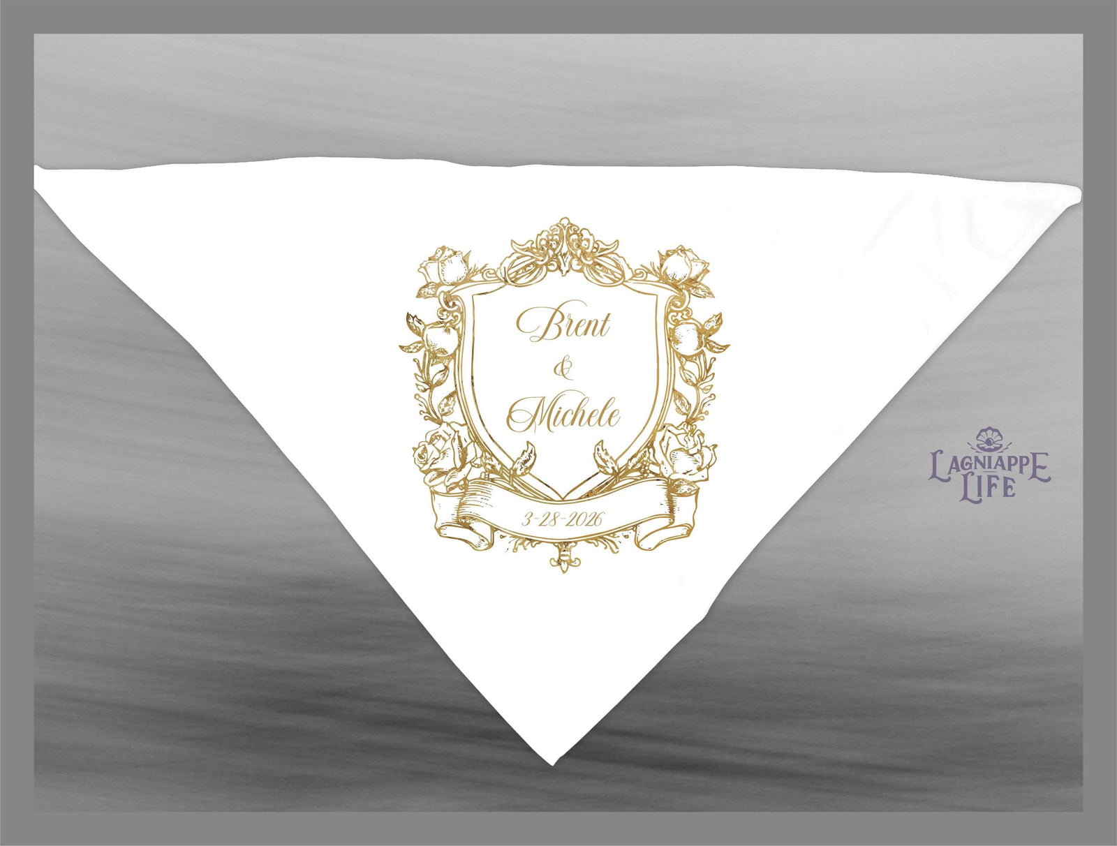 May include: A white wedding favor with a gold crest design. The crest features a shield with the names 'Brent & Michele' and the date '3.18.2018'. The crest is surrounded by floral designs and a banner. The text 'Lagniappe Life' is in the lower right corner of the favor.